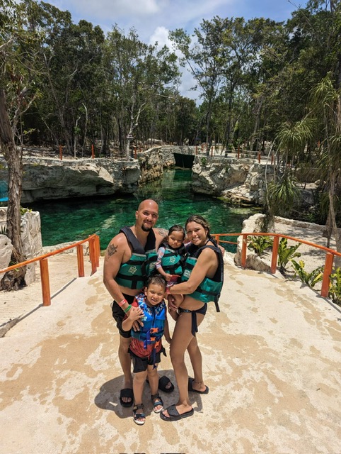 Samantha and her family embrace happily with life vests near palm trees and water.