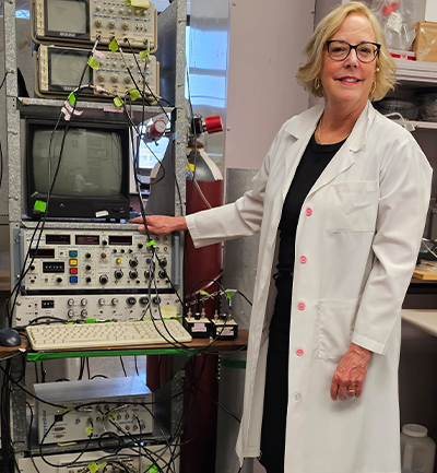 Dr. Howlett stands next to research equipment in her lab