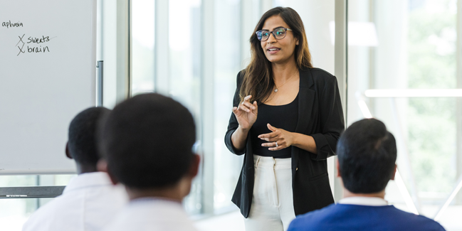 A woman of colour lectures to a small group of medical students.