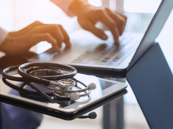 A laptop, a tablet, a computer and a stethoscope on a table