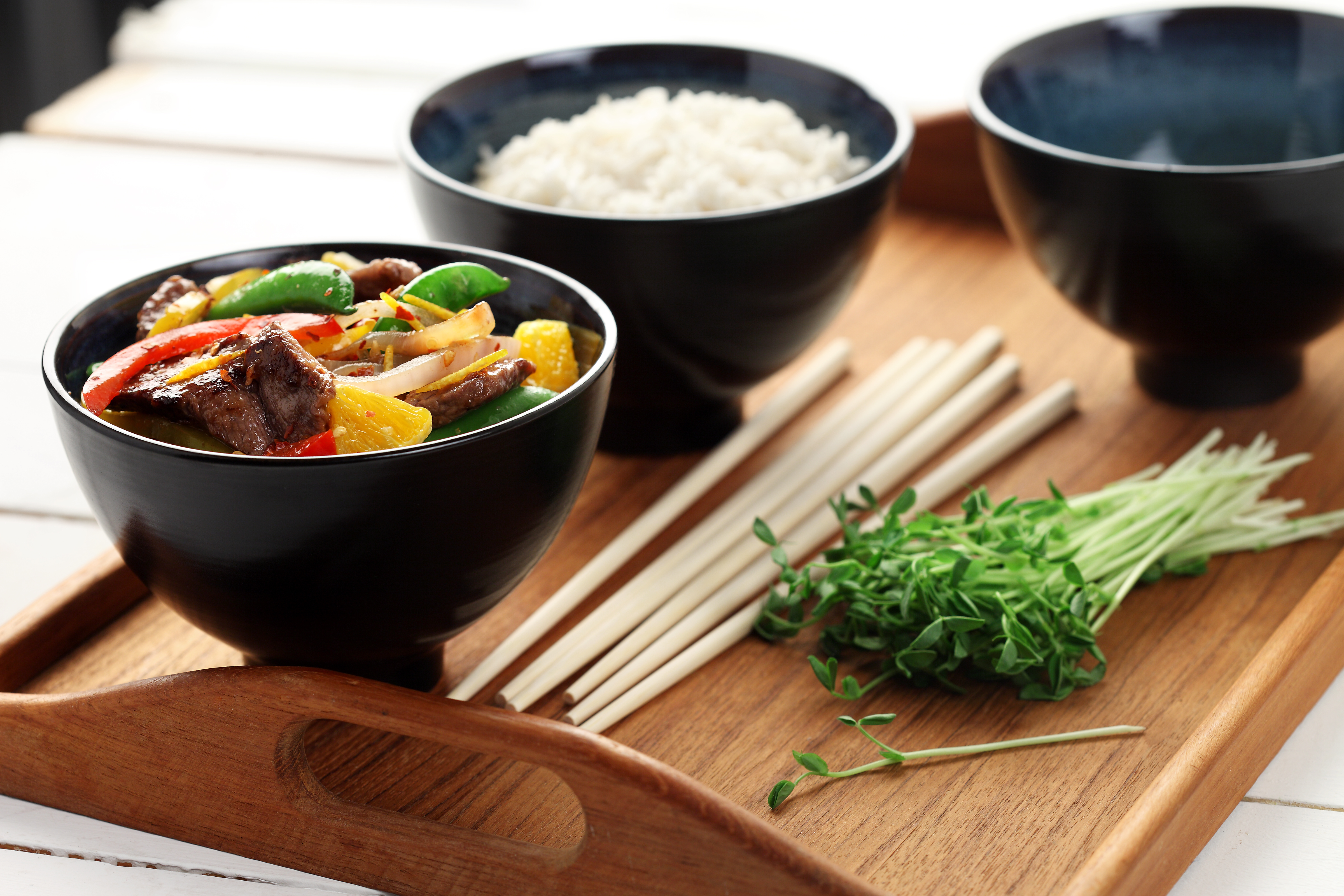 Spicy beef with oranges in black bowls on a wooden tray