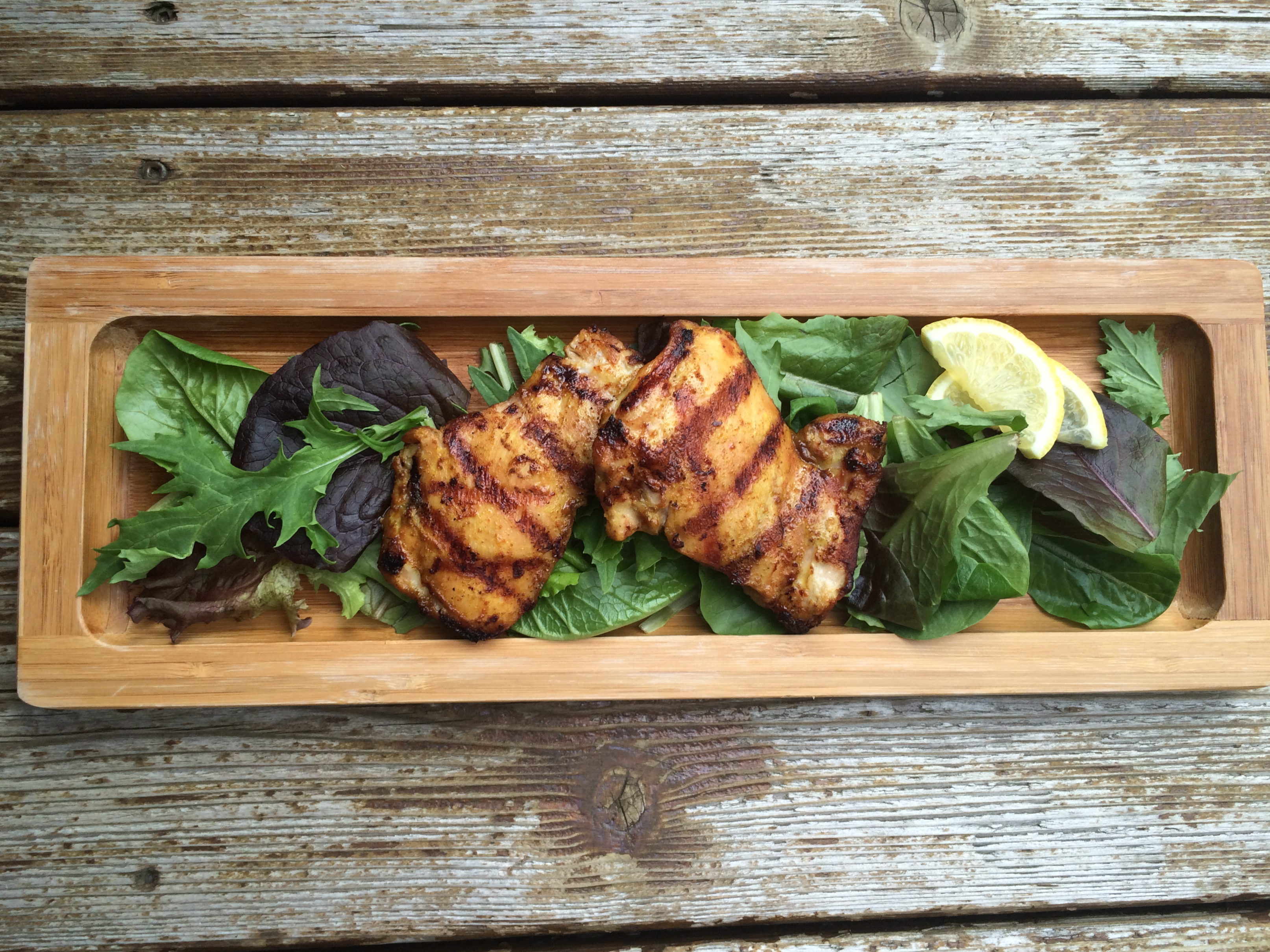 Zippy chicken thighs for the grill on a wooden plank.